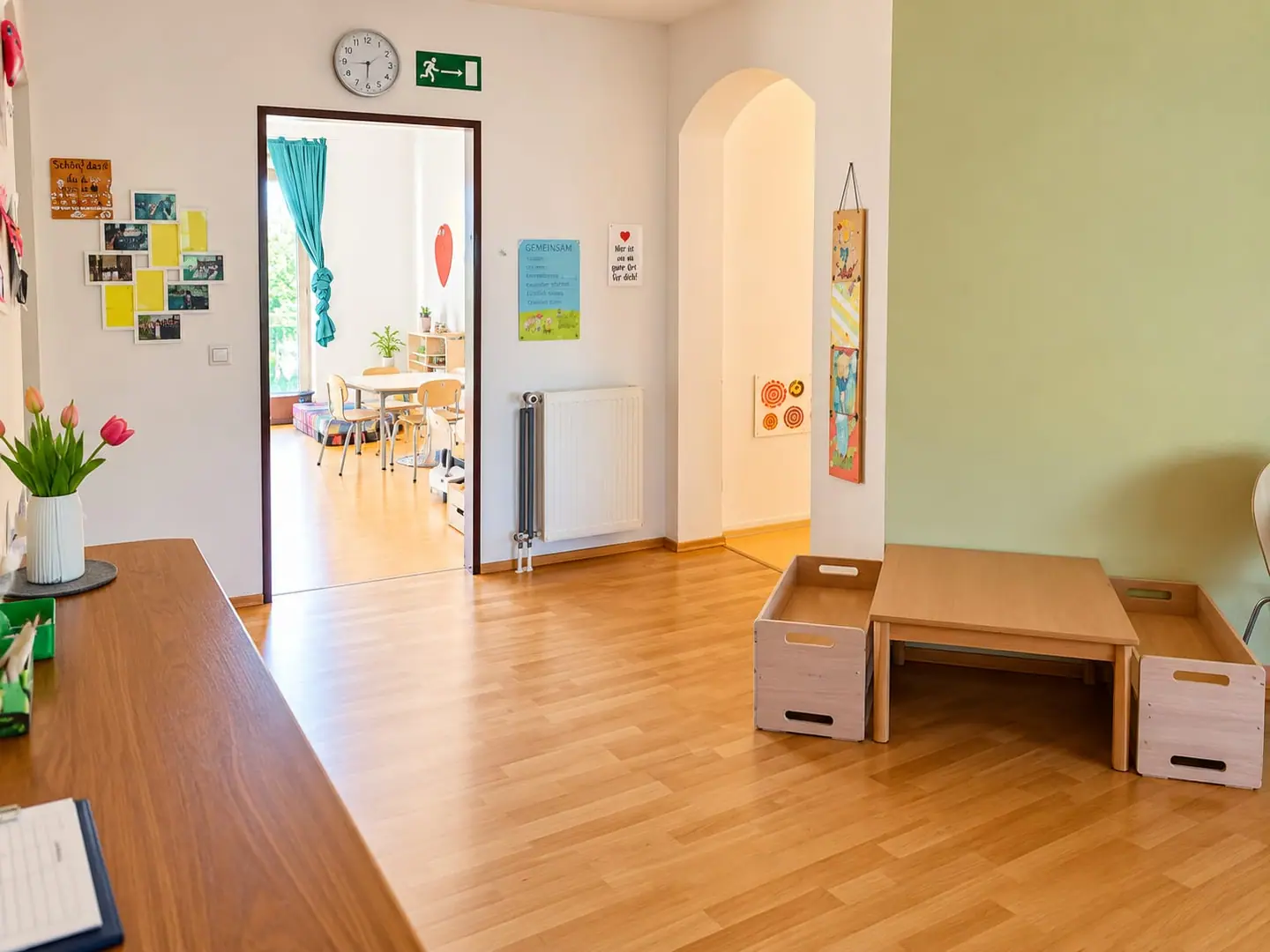 Heller Eingangsbereich mit Holzboden, Kindertisch und Tulpen; durch die offene Tür sieht man ins Spielzimmer.