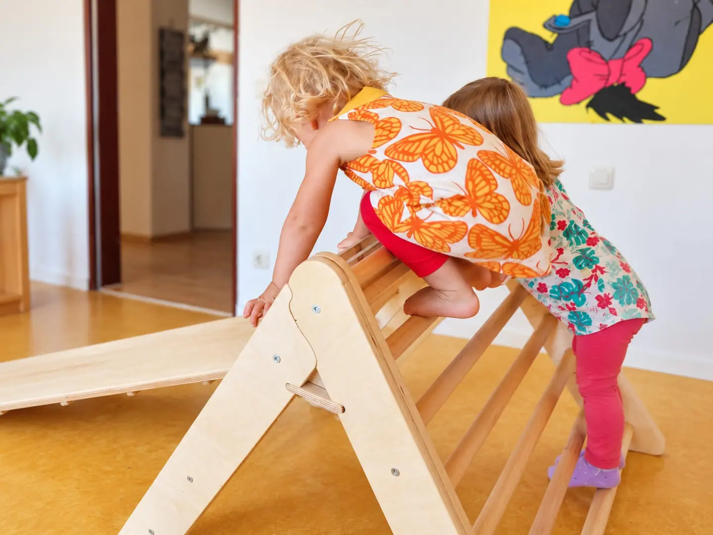Zwei Kleinkinder klettern gemeinsam über ein Kletterdreieck aus Holz.